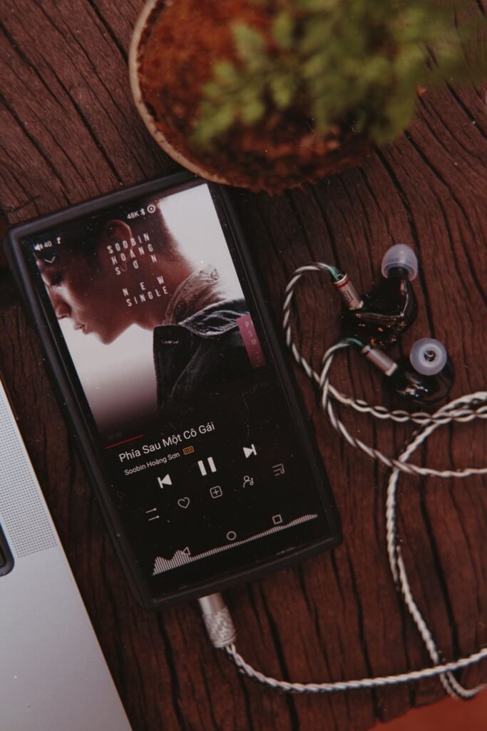 pexels-photo-34974213-34974213 A smartphone with earphones playing a song on a wooden table next to a plant.